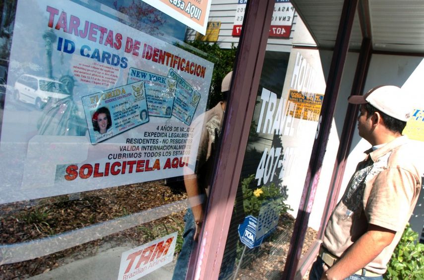 Una persona de pie frente a un anuncio de venta de tarjetas de identificación y licencias. (EFE)