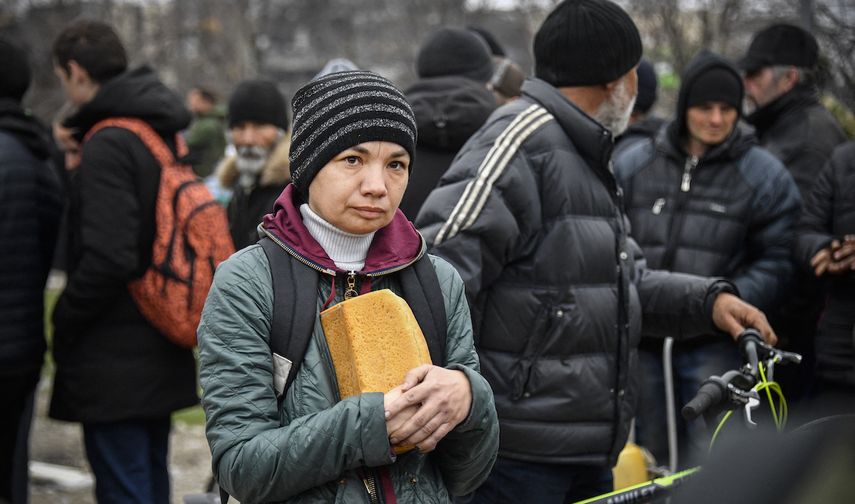 Una mujer sostiene un pan mientras la gente espera en fila en una distribución de alimentos organizada por el ejército ruso y voluntarios en Mariupol el 12 de abril de 2022, mientras las tropas rusas intensifican una campaña para tomar la ciudad portuaria estratégica, parte de un ataque masivo anticipado en el este de Ucrania.