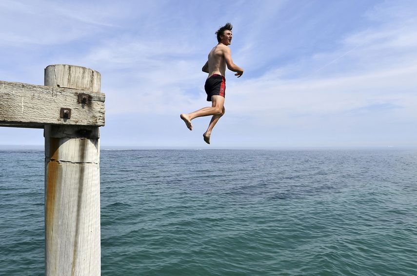 En esta imagen del martes 17 de diciembre de 2019, un nadador salta al agua desde un muelle del puerto de Noarlunga Jetty, en un intento de refrescarse en Adelaida, Australia.&nbsp;
