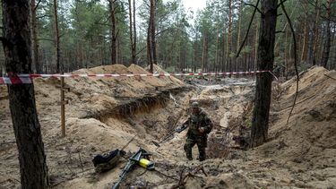 Un soldado ucraniano usa un detector de metal para inspeccionar una fosa común en el área metropolitana de la ciudad de Izium, en Ucrania, el jueves 15 de septiembre de 2022