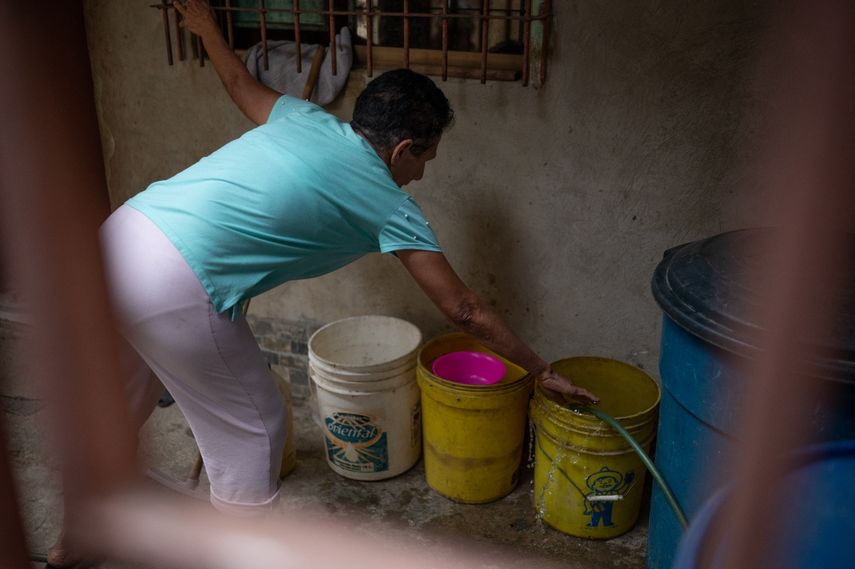 Una mujer llena recipientes de plástico con agua en su manguera en el barrio La Vega en Caracas, el 9 de agosto de 2023.