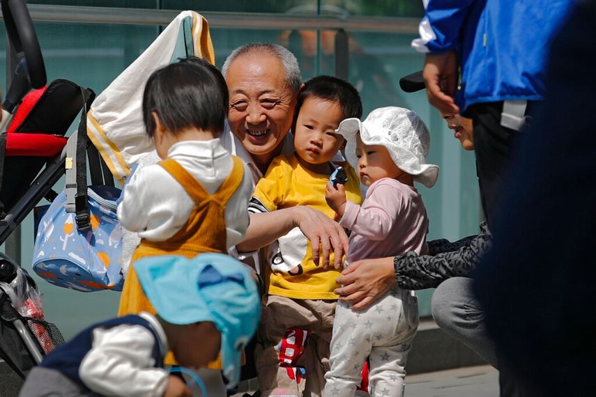 Un anciano juega con niños cerca de un edificio de oficinas en Beijing, el 10 de mayo de 2021. El gobierno chino relajará los límites de natalidad para permitir que todas las parejas puedan tener tres hijos en lugar de dos para hacer frente al rápido envejecimiento de la población, según dijo el lunes 31 de mayo una agencia estatal de noticias.