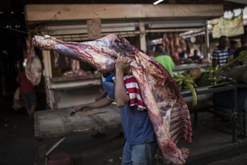 Un vendedor carga con una pieza de carne en una carnicería en un mercado de Maracaibo, Venezuela. Tendrá que venderla pronto ya que, sin refrigeración, los alimentos perecederos se estropean rápidamente.