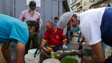 Personas usan mascarillas y pa&ntilde;uelos como medida preventiva contra la pandemia mundial de coronavirus COVID-19 mientras recolectan agua de una tuber&iacute;a de la calle en Caracas, el 21 de marzo de 2020.