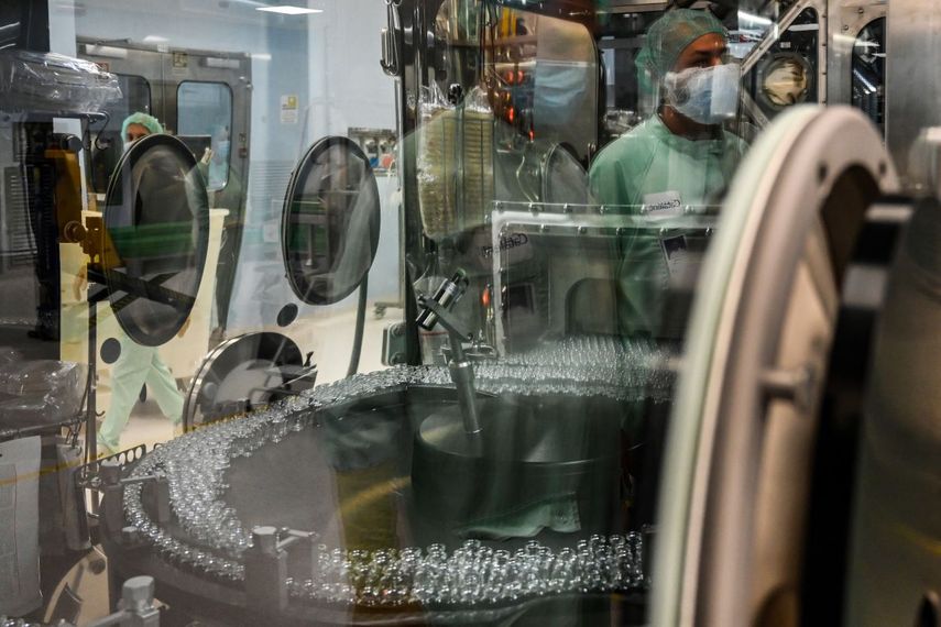 Un técnico de laboratorio, cuyo reflejo puede verse (Arriba a la derecha) supervisa las pruebas de llenado y envasado para la producción y suministro a gran escala de la vacuna candidata COVID-19 de la Universidad de Oxford, AZD1222, el 11 de septiembre de 2020 en una planta de fabricación de productos biológicos de la corporación multinacional Catalent en Anagni, al sureste de Roma, Italia.