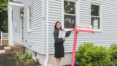 Una agente de bienes raíces frente a una casa pendiente a ser comprada.