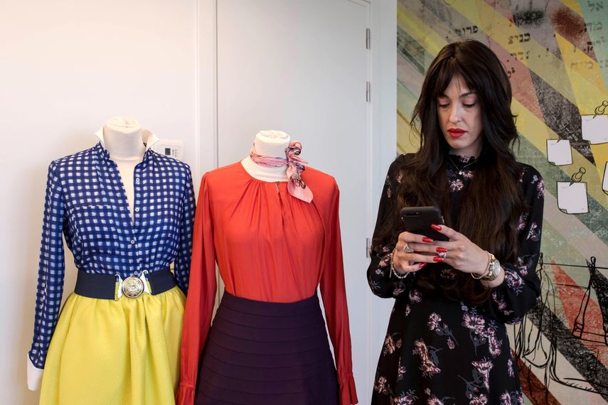 Miri&nbsp;Beilin, estilista y profesora de moda haredi, ojea su móvil en la escuela de diseño Hani Dobkin, junto a dos creaciones ideadas para las mujeres ultraortodoxas.