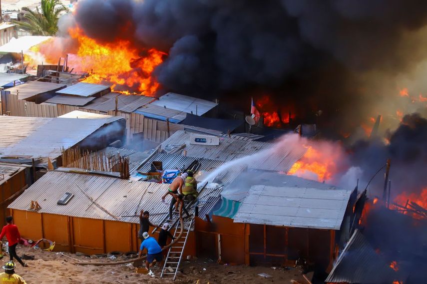 Vecinos ayudan a combatir un incendio en el barrio de escasos recursos de Laguna Verde, en Iquique, Chile, el lunes 10 de enero de 2022