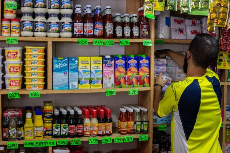Un empleado de una tienda organiza productos alimenticios en un estante con los carteles de precios de los productos en bolívares en Caracas, Venezuela el 28 de septiembre de 2021.
