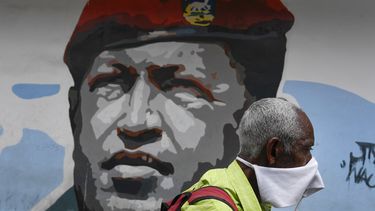 Un hombre que porta una mascarilla improvisada para protegerse del coronavirus camina el domingo 29 de marzo de 2020 junto a un mural del fallecido Hugo Chávez, en Caracas, Venezuela