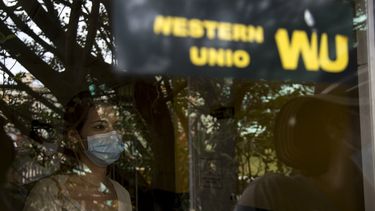 Fotografiada a través de una ventana, una mujer aguarda a cobrar en una oficina de Western Union durante su último día de operaciones en La Habana, Cuba, el lunes 23 de noviembre de 2020. Cuba iniciará un reordenamiento económico profundo a partir del 1 de enero que incluirá la unificación monetaria y cambiaria, así como un aumento de cinco veces en los salarios.