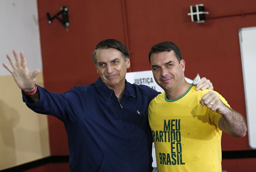 &nbsp;El presidente Jair Bolsonaro, izquierda, y su hijo Fl&aacute;vio saludando a reporteros en un centro de votaci&oacute;n en R&iacute;o de Janeiro, Brasil, momentos antes de su elecci&oacute;n como presidente. 7 de octubre de 2018.&nbsp;&nbsp;   &nbsp;