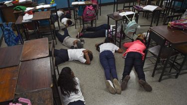 Los alumnos se cubren la cabeza mientras yacen en el suelo durante un simulacro de tiroteo en la escuela Manuel Aguirre en el barrio La Bombilla en Caracas el 23 de febrero de 2023. Simulacros de tiroteos organizados por el Comité Internacional de la Cruz Roja (CICR) se están llevando a cabo en escuelas de algunos de los barrios más violentos de Caracas.