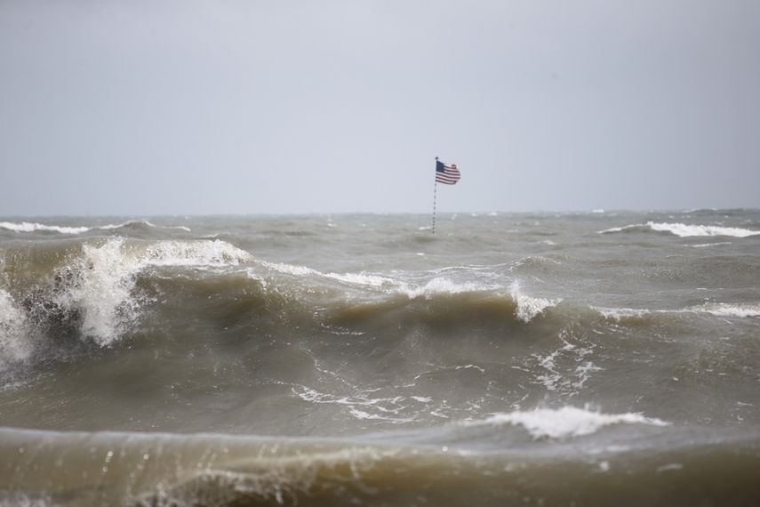 Olas impulsadas por los vientos de Dorian rompen frente a un embarcadero en Vero Beach, Florida, donde alguien plantó una bandera de EEUU.