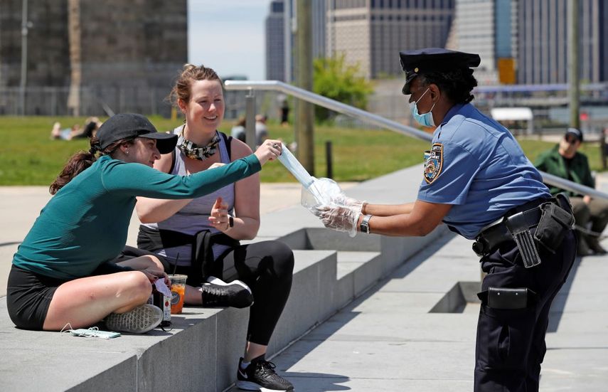 &nbsp; La agente Bynoe, derecha, del Grupo de Seguridad Escolar del Departamento de Polic&iacute;a de Nueva York, proporciona cubrebocas a un par de mujeres en el Parque Brooklyn Bridge como medida para frenar la propagaci&oacute;n del nuevo coronavirus, el domingo 17 de mayo de 2020, en Nueva York.