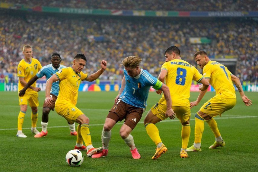 El belga Kevin De Bruyne pelea por mantener el control del balón entre los ucranianos Ruslan Malinovskyi y Andriy Yarmolenko en el encuentro del Grupo E de la Eurocopa el miércoles 26 de junio del 2024.&nbsp;