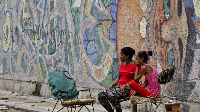 Dos mujeres sentadas frente a una pared decorada con graffitis en La Habana, Cuba, en agosto de 2018.