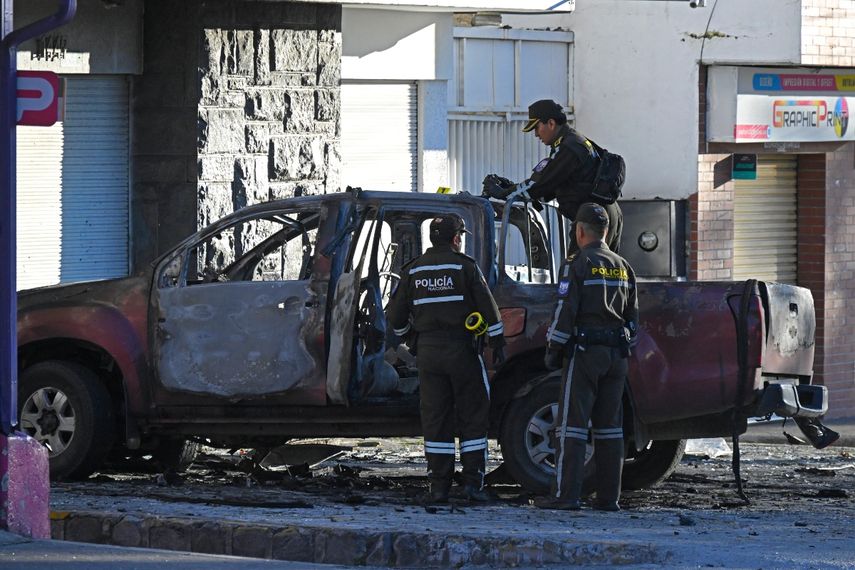 Policías inspeccionan los restos de un auto quemado frente a la sede del organismo encargado de la gestión penitenciaria (SNAI) el 31 de agosto de 2023 en Quito.