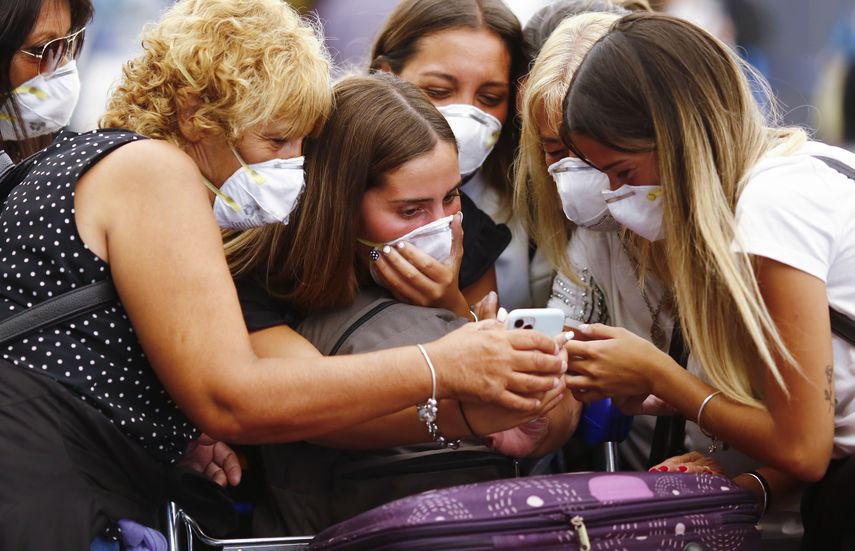 Viajeros con m&aacute;scaras protectoras miran un tel&eacute;fono inteligente en el Aeropuerto Internacional Ministro Pistarini, en Ezeiza, en las afueras de Buenos Aires, Argentina, el viernes 13 de marzo de 2020.&nbsp;