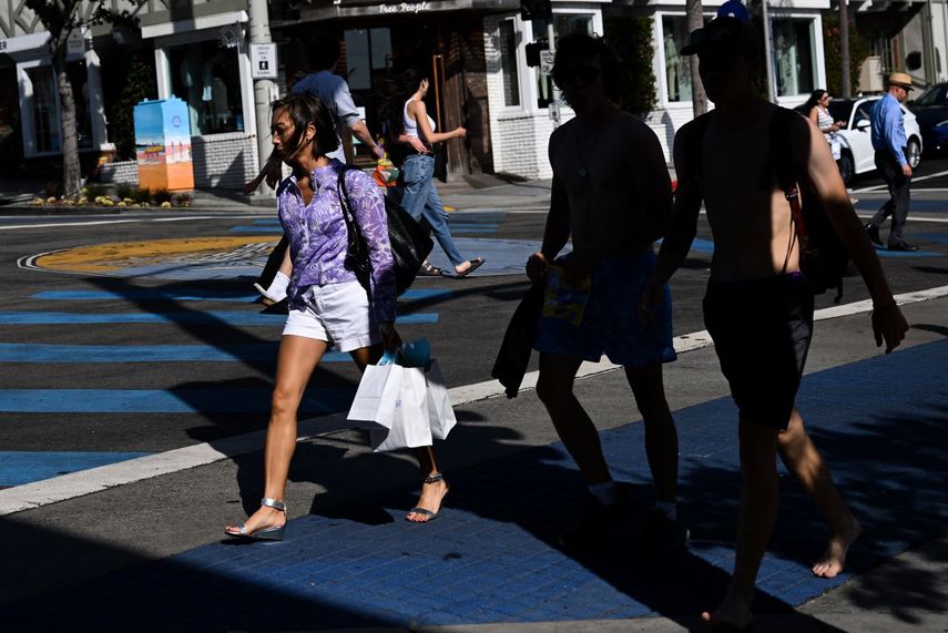 Una mujer cargas bolsas de compras mientras cruza una calle en Manhattan Beach, California.
