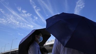 Gente cubriéndose con paraguas bajo un cielo azul con algunas nubes en un día caluroso en Beijing, el jueves 14 de julio de 2022.&nbsp;