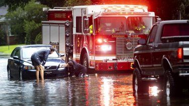 Dos personas atan un cabo a un auto varado en una calle anegada debido a las fuertes lluvias de la tormenta tropical Debby, el 5 de agosto de 2024, en Savannah, Georgia.&nbsp;
