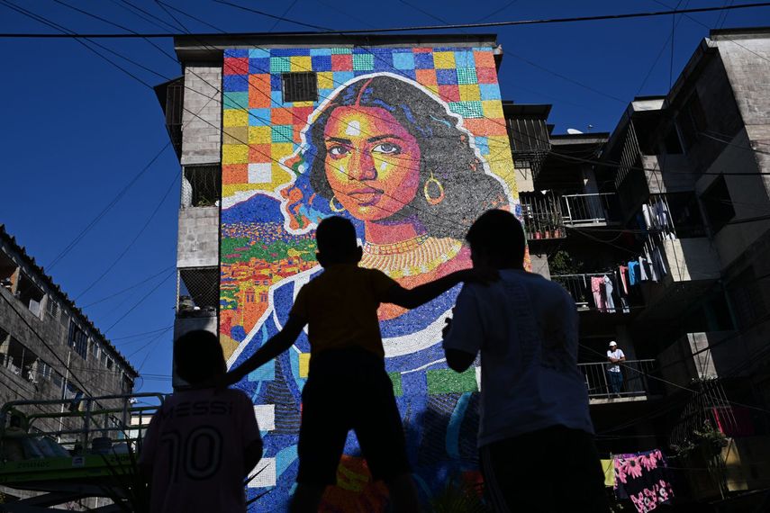 Niños miran un mural hecho con tapas de botellas de plástico por el artista venezolano Oscar Olivares en un edificio de apartamentos en el barrio Zacamil en Mejicanos, El Salvador, el 20 de febrero de 2026.