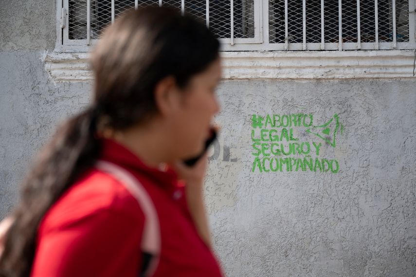 Una mujer usa su teléfono móvil mientras pasa frente a un grafiti a favor de la legalización del aborto pintado por organizaciones feministas en Caracas, Venezuela.