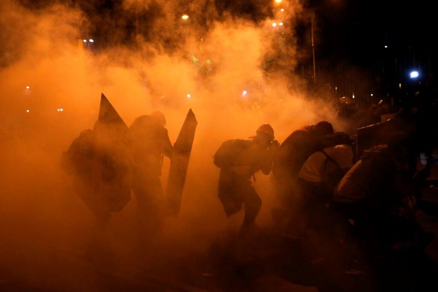 Manifestantes buscan resguardo del gas lacrimógeno lanzado por la policía durante las protestas en Lima, Perú.