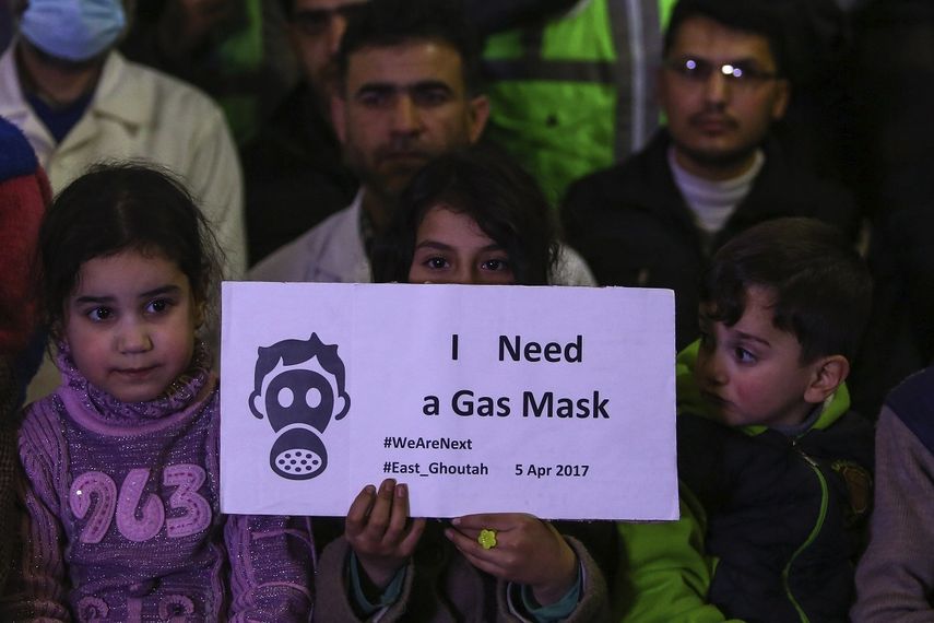 Niños sirios, junto con voluntarios y personal de primeros auxilios muestran pancartas durante una concentración en Douma para mostrar solidaridad con los fallecidos durante el ataque químico del martes pasado.