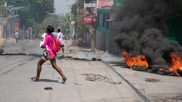 Una mujer con un niño en brazos corre por una calle de Puerto Príncipe, en medio de disturbios provocados por las pandillas.