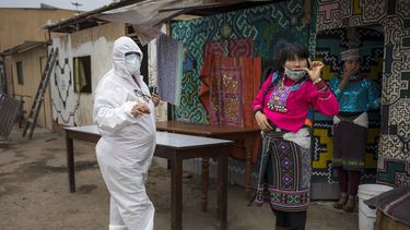 Olinda Silvano, de la etnia shipibo conibo, habla con una trabajadora de una ONG ataviada con ropa de protecci&oacute;n contra el nuevo coronavirus, durante las celebraciones del d&iacute;a de San Juan, santo patr&oacute;n de la Amazon&iacute;a peruana, en el barrio de Cantagallo, en Lima, Per&uacute;, el mi&eacute;rcoles 24 de junio de 2020. (AP Foto/Rodrigo Abd