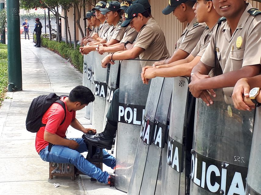 Un limpiabotas ambulante limpia los zapatos de un policía, mientras estos protegen el centro de convenciones donde se realiza la VIII Cumbre de las Américas, en Lima.