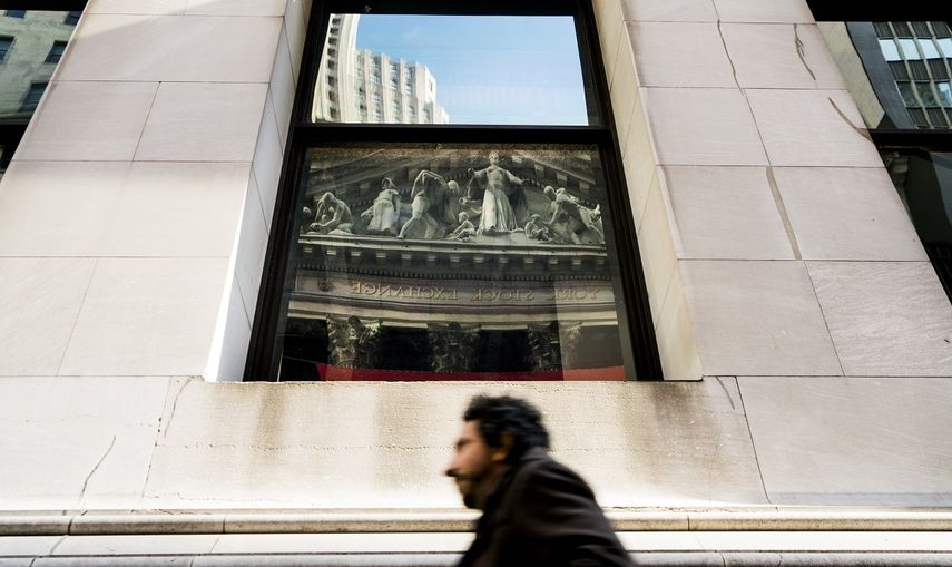 Un hombre camina frente una ventana donde se refleja la Bolsa de Nueva York, EEUU.