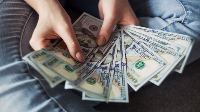Una mujer muestra billetes de dólar estadounidense.