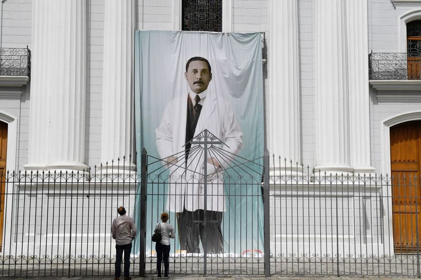 En esta foto de archivo tomada el 21 de junio de 2020, la gente observa la imagen del médico venezolano José Gregorio Hernández, en la parte exterior de la iglesia La Candelaria, que guarda sus restos, en Caracas.