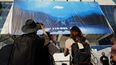 La gente toma fotografías mientras los trabajadores cuelgan el cartel oficial del 77º Festival de Cannes en la fachada del Palacio de Festivales en Cannes, sureste de Francia, el 12 de mayo de 2024. El Festival se llevará a cabo del 14 al 25 de mayo. &nbsp;