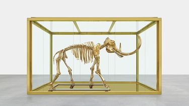 En esta imagen difundida por Damien Hirst and Science Ltd., la más reciente obra del artista británico Damien Hirst, Gone but Not Forgotten (Desaparecido pero no olvidado), muestra a un mamut de lana enchapada en oro en una vitrina dorada. La pieza s