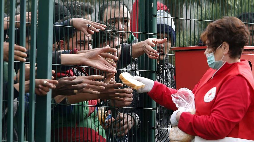 Una trabajadora de la Cruz Roja ofrece pan a los refugiados tras una valla en el campo de refugiados en&nbsp;Eslovenia&nbsp;