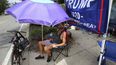 Ray Renaud, de Daytona Beach, Florida, se cubre con una sombrilla mientras simpatizantes del presidente Donald Trump acampan frente al Amway Center el lunes 17 de junio de 2019, antes de un evento para dar inicio a la campaña de reelección 2020 en Orlando, Florida.