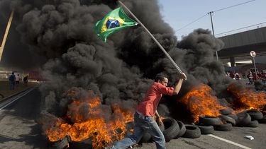 Un integrante del grupo Movimiento de Trabajadores sin Techo porta una bandera brasileña frente a neumáticos quemados en una protesta contra el dinero gastado en el Mundial, en Sao Paulo, cerca del estadio Itaquerao. (AP)