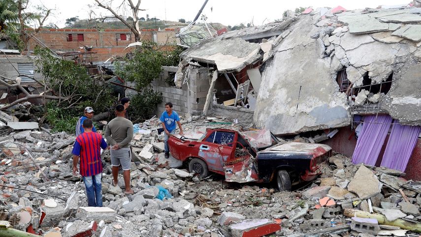 Varias personas miran el estado en que quedó un auto aplastado por los escombros, en el municipio de Regla, tras el paso de un tornado en La Habana.