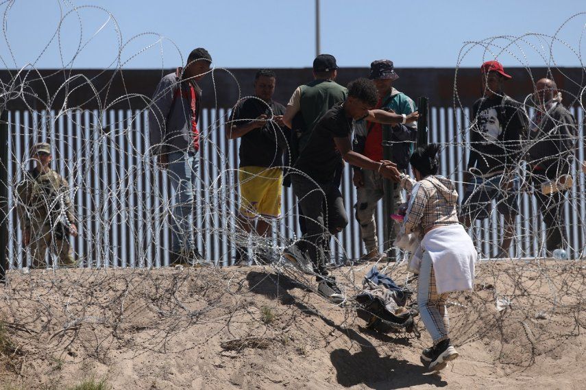 Migrantes se acercan al muro fronterizo ante la mirada de un efectivo de la Guardia Nacional.