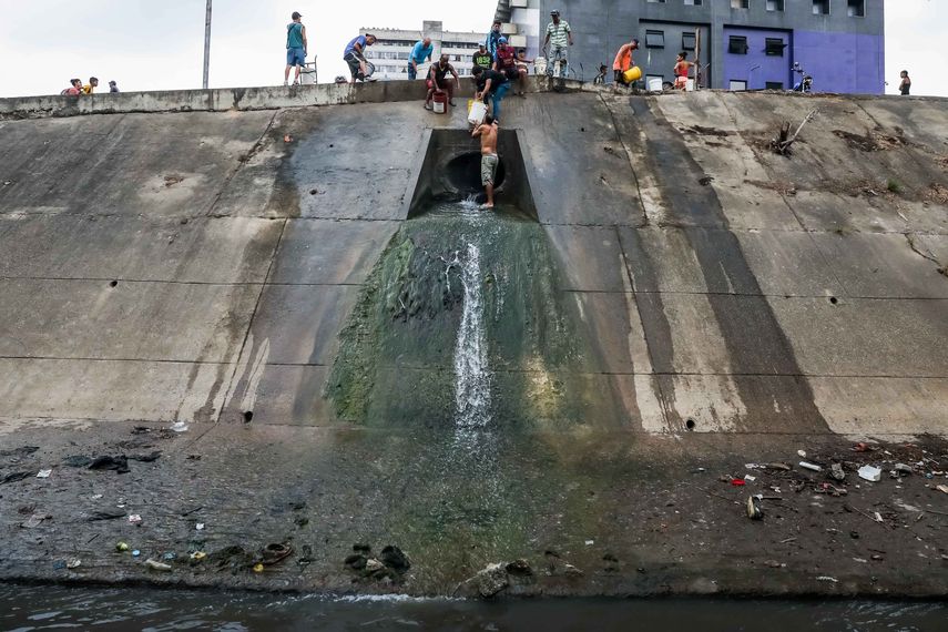 Un grupo de personas recoge agua desde una tubería de desagüe en la orilla del contaminado Río Guaire, en Caracas.