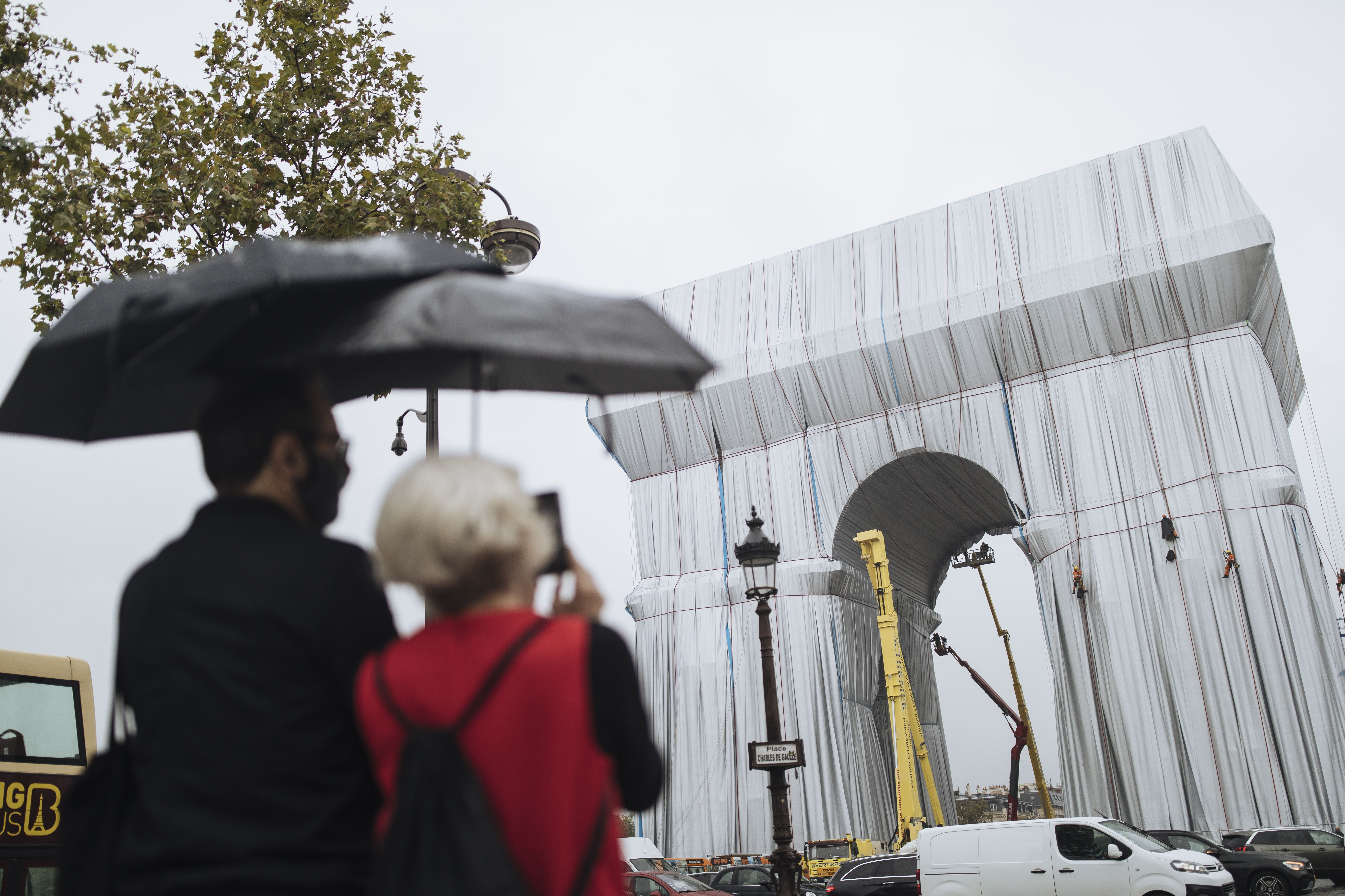 Dos personas miran cómo varios trabajadores envuelven en tela el monumento del Arco de Triunfo, en París, el miércoles 15 de septiembre de 2021. Dos personas miran cómo varios trabajadores envuelven en tela el monumento del Arco de Triunfo, en París, el miércoles 15 de septiembre de 2021.