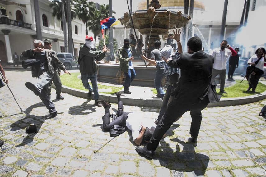 El diputado Armando Armas (c) es golpeado por manifestantes en el piso en la Asamblea Nacional.&nbsp;