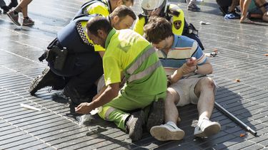 Una persona es ayudada por policías españoles y dos hombres después de que una camioneta se estrellara contra la multitud en Las Ramblas de Barcelona en 2017.