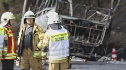 Los bomberos atienden la emergencia, mientras al fondo se ve el bus totalmente quemado.&nbsp;