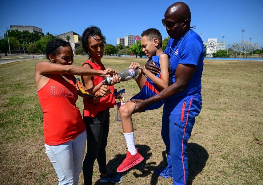 El pequeño Juan José Guilarte, de Cuba, es cargado por su entrenador Albert Luis Campbell (derecha), mientras que su abuela Suleimi Licea Rodríguez (izquierda) y su madre Sheila Guilarte ajustan su prótesis, el 16 de abril de 2026.