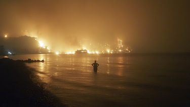 Imagen del viernes 6 de agosto de 2021, un hombre mira desde el agua cómo los incendios se acercan a la playa de Kochyli, cerca del poblado de Limni, en la isla griega de Evia, unos 160 kilómetros (100 millas) al norte de Atenas, Grecia.&nbsp;